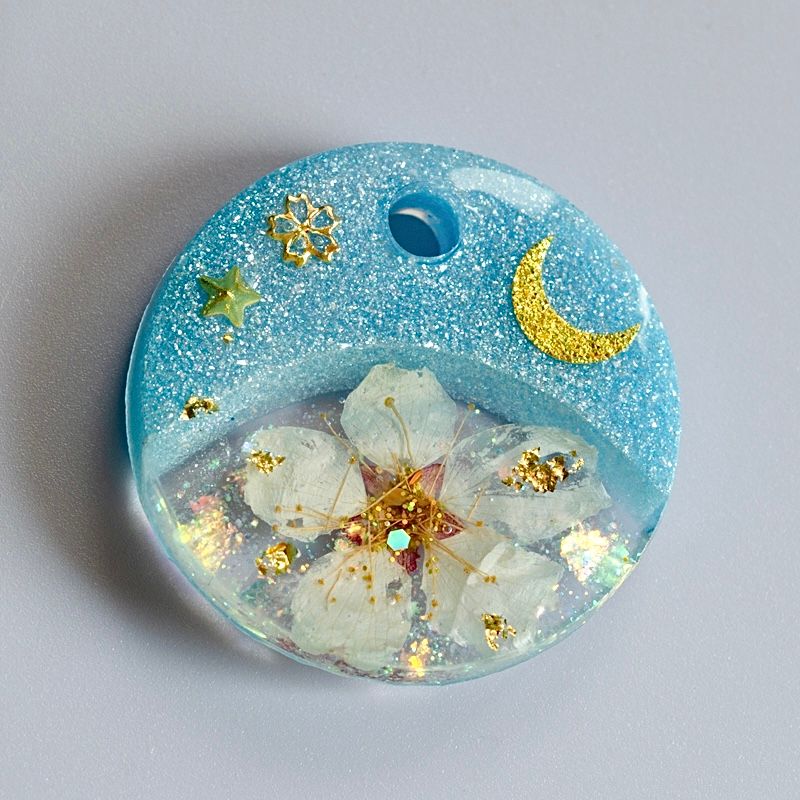 A picture of Hundemarke mit einer echten Kirschblüte und Glitzerakzenten. Mond und Sterne sowie feines Blattgold bringen einen zauberhaften Look. In rosa oder blau erhältlich und limitiert auf insgesamt vier Stück (jeweils eine Marke für Version A, B, C und D).