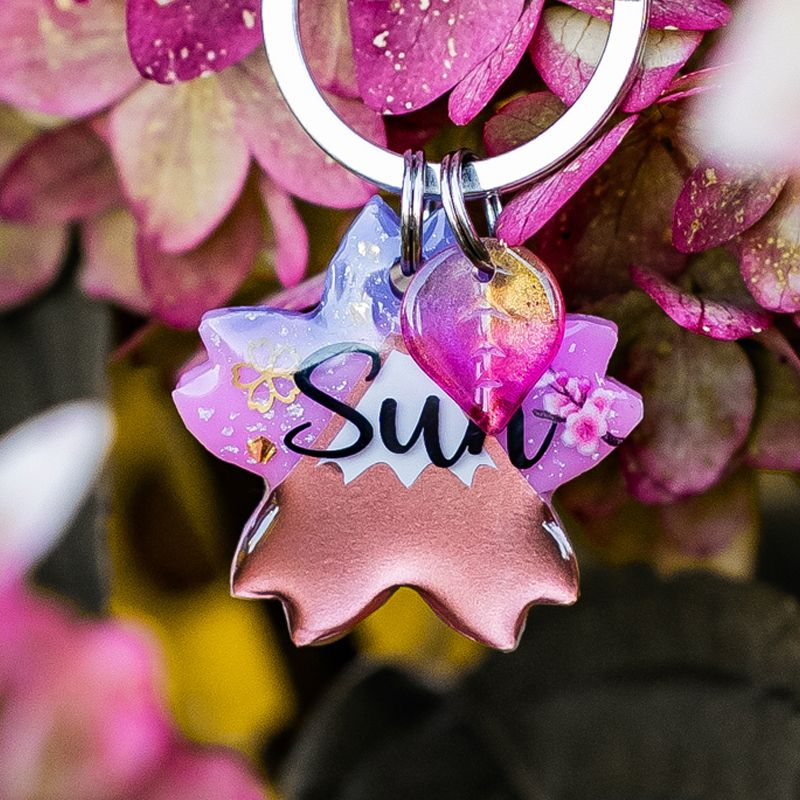 A picture of Unsere Fujizakura-Marke in einer neuen und besonderen Variante: das Fuji-Motiv erstrahlt hier in Roségold, vor einem sanft gesprenkelten Himmel, umgeben von rosa Blüten und funkelnden Goldakzenten. 🌸✨