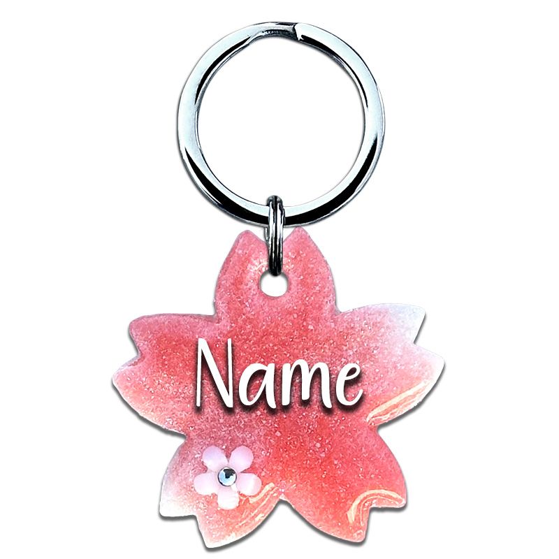 A picture of Für alle, die Schlichtheit und Eleganz lieben. Diese Tiermarke in Form einer zarten Kirschblüte besticht durch pinkes Perlpigment, das harmonisch mit weißen, glitzernden Akzenten kombiniert wird. Das Highlight des Designs ist die kleine weiße Blüte, die mit funkelndem Glitzer verziert ist – ein echter Hingucker für jeden, der etwas Besonderes sucht.